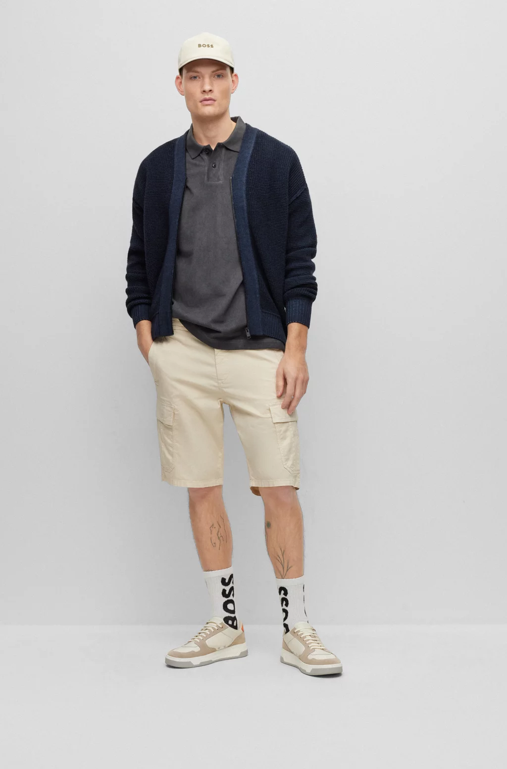 A man wearing a blue cardigan, beige shorts, and sneakers